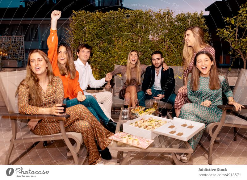 Vergnügte Freunde bei einer Party auf der Terrasse Spaß haben Menschengruppe Abendessen feiern positiv Sitzung Bonden Zeit verbringen genießen Snack Schnaps