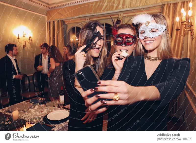 Positive Frauen in Karnevalsmasken machen ein Selfie im Restaurant Selbstportrait Abendessen Maskerade Mundschutz Freund Spaß haben soziale Netzwerke Anlass
