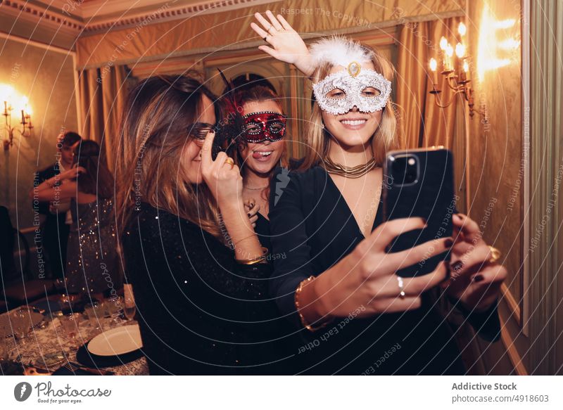 Positive Frauen in Karnevalsmasken machen ein Selfie im Restaurant Selbstportrait Abendessen Maskerade Mundschutz Freund Spaß haben soziale Netzwerke Anlass