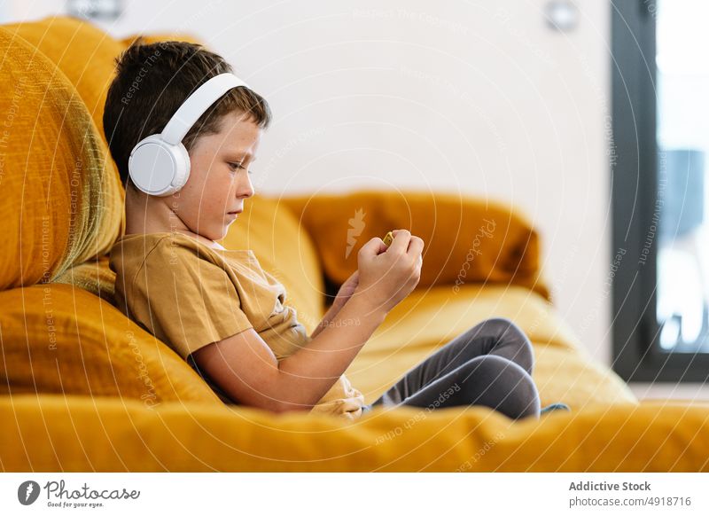 Junge auf einem Sofa sitzend, der ein Mobiltelefon benutzt Kind heimwärts Handy Technik & Technologie Smartphone Kopfhörer jung zuhören ernst konzentriert Film