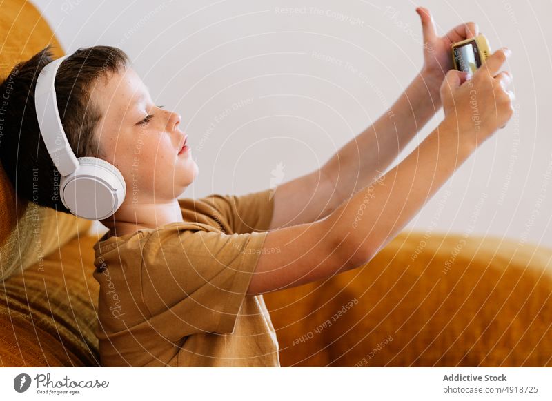 Junge auf einem Sofa sitzend mit Kopfhörern und einem Mobiltelefon Kind heimwärts Telefon Technik & Technologie im Innenbereich jung Menschen ernst konzentriert