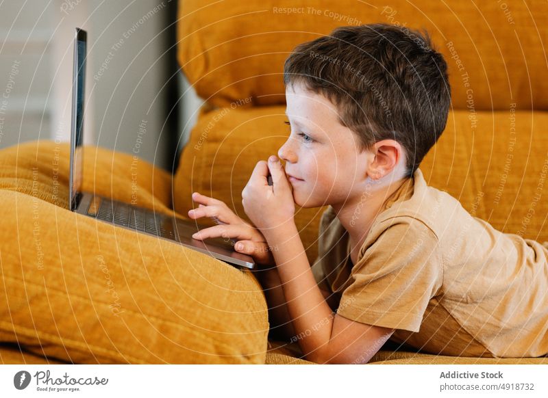 Junge auf einem Sofa liegend, der den Laptop benutzt Kind Computer Glück Kaukasier Technik & Technologie männlich Lächeln im Innenbereich heimwärts Kindheit