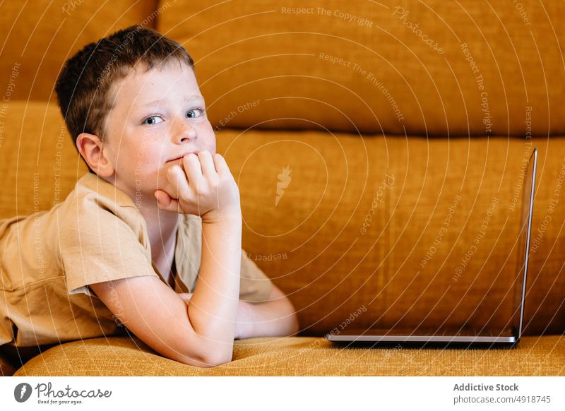 Junge auf einem Sofa liegend, der den Laptop benutzt Kind Computer nachdenklich Kaukasier Technik & Technologie männlich im Innenbereich heimwärts Kindheit