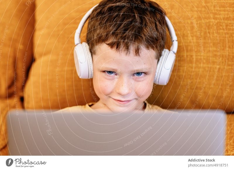 Junge sitzt auf einem Sofa mit Kopfhörern auf dem Kopf und benutzt den Laptop Kind Lächeln Computer Glück Kaukasier Technik & Technologie männlich Karikatur