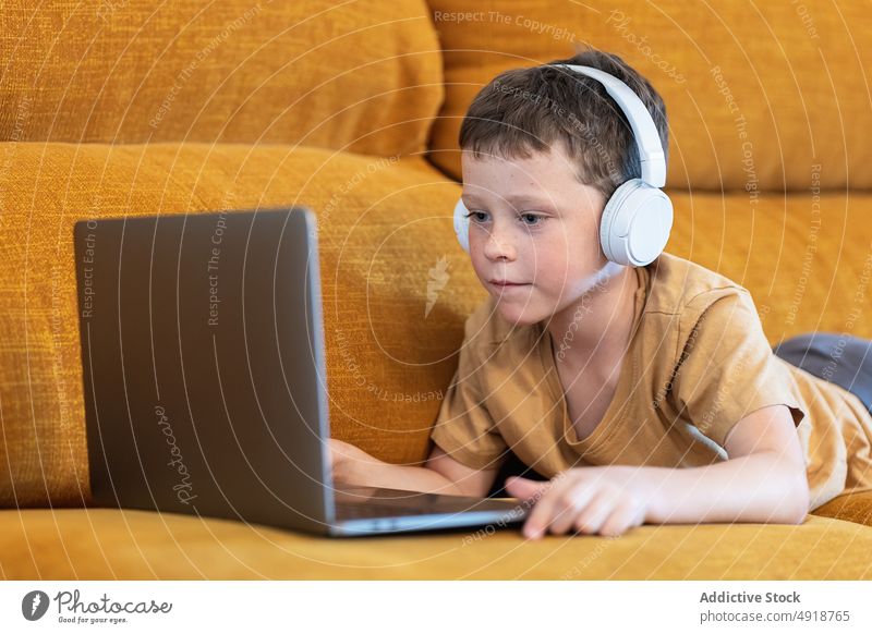 Junge sitzt auf einem Sofa mit Kopfhörern auf dem Kopf und benutzt den Laptop Kind Computer Kaukasier Technik & Technologie männlich ernst Konzentration