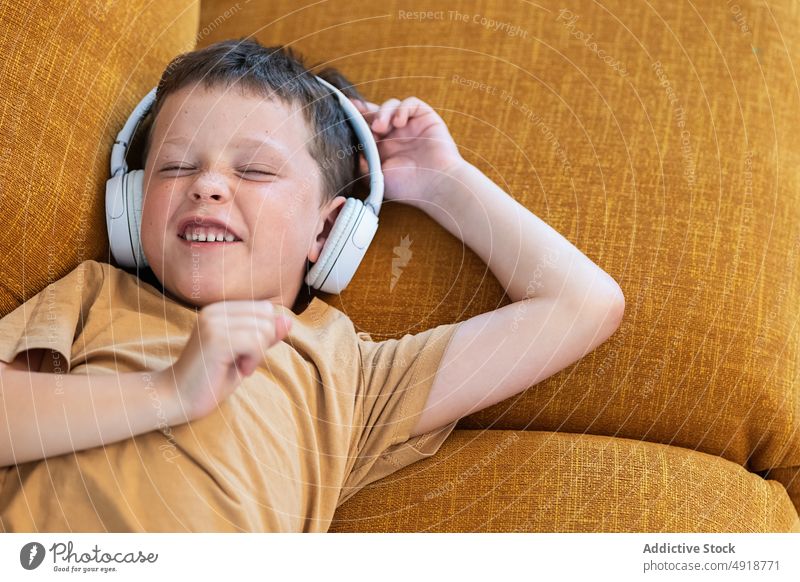Glücklicher Junge auf dem Sofa liegend mit geschlossenen Augen Kind Kopfhörer Wiedergabeliste heimwärts gelangweilt Augen geschlossen Musik