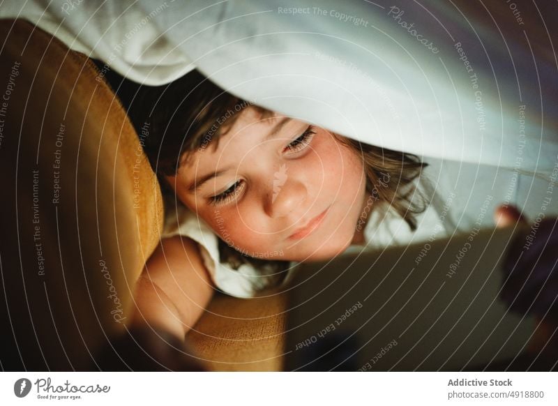 Mädchen unter einer Decke, das ein Mobiltelefon benutzt Kind heimwärts Technik & Technologie im Innenbereich Licht jung Browsen konzentriert Karikatur Lügen