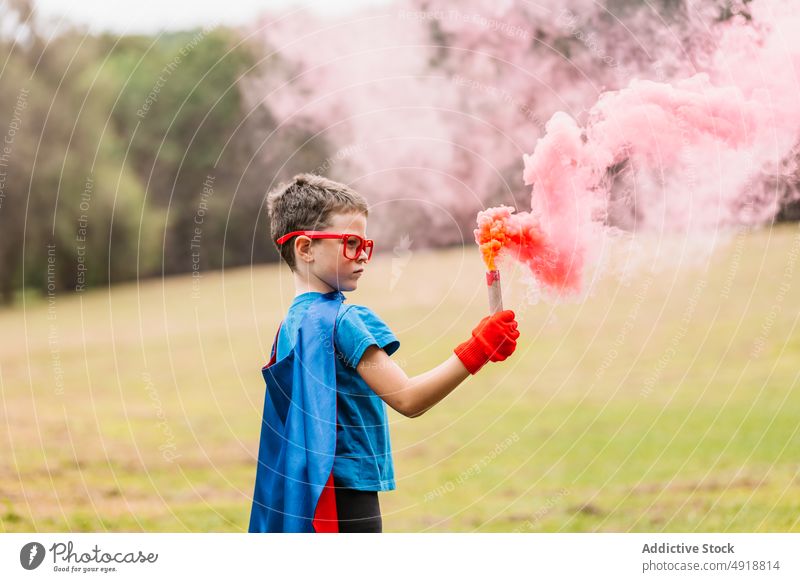 Kleiner Superheld mit Rauchbombe Junge Park Tracht spielen Kraft Fokus Rasen farbenfroh hell Kind Vorstellungskraft Phantasie bezaubernd Sommer pulsierend