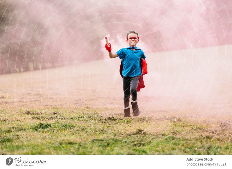 Kleiner Superheld mit Rauchbombe läuft herum Junge Park aufgeregt Tracht spielen Kraft Rasen laufen farbenfroh hell Lächeln Kind Glück Vorstellungskraft