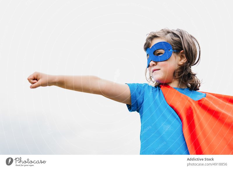 Aufgeregtes Mädchen im Superheldenkostüm im Park spielen Baum Tracht Arm angehoben Held Kraft wolkig Frau Kap Mundschutz aufgeregt Sommer Kind tagsüber Mut