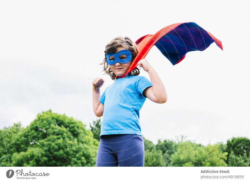 Aufgeregtes Mädchen im Superheldenkostüm im Park spielen Baum Tracht Arm angehoben Held Kraft wolkig Frau Kap Mundschutz aufgeregt Sommer Kind tagsüber Mut
