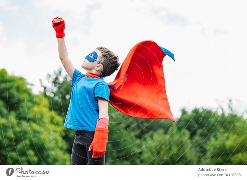 Aufgeregter Junge im Superheldenkostüm im Park schreien spielen Baum Tracht Arm angehoben Held Kraft wolkig Kap Mundschutz aufgeregt Sommer Kind tagsüber Mut