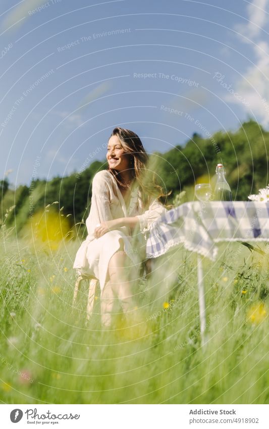 Positive Frau sitzt am Tisch in einem Feld Picknick Landschaft Sommer Erholung Natur Gras Zeitvertreib ruhen feminin Lächeln Getränk Kleid Optimist Inhalt