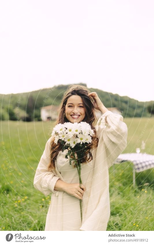 Lächelnde Frau mit Blumen im Feld stehend Blumenstrauß Landschaft Gras Erholung Sommer Haufen Natur Zeitvertreib feminin Tisch Freude geblümt Pflanze Umwelt