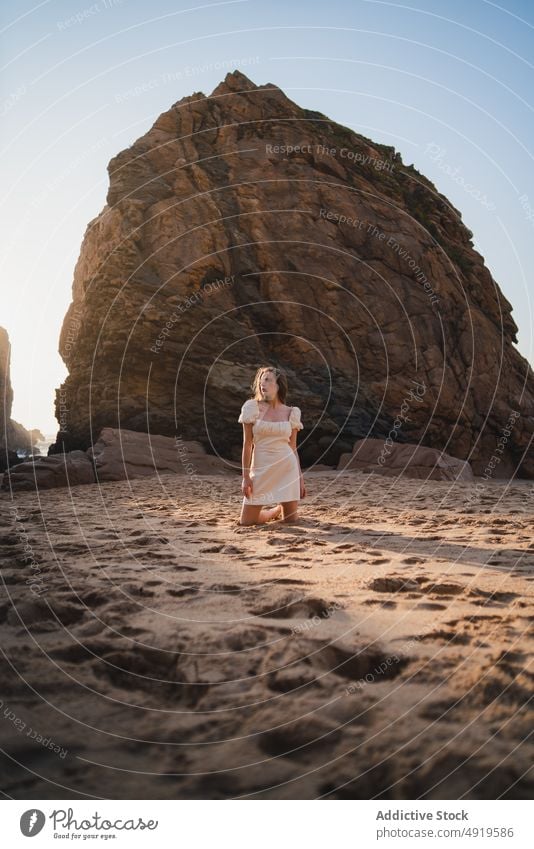 Frau sitzend am Strand mit Felsen Reisender MEER Wasser Ufer Sonnenuntergang Zeitvertreib Fernweh Stein feminin Kleid genießen Anmut Ausflug ruhen Sonnenlicht