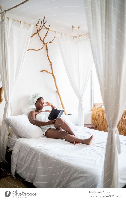 Schwarze Frau liegt auf einem Bett und liest ein Buch schwarz Notebook lesen Pflege Schönheit Erholung Therapie jung Spa schön sich[Akk] entspannen Wellness
