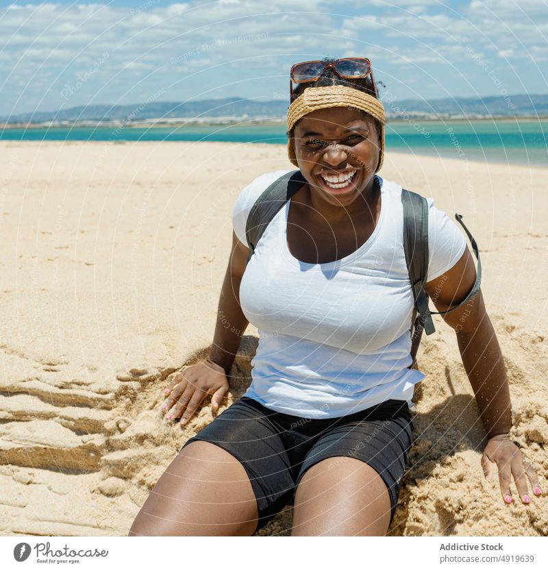 Schwarze Frau lächelnd auf dem Sand am Strand sitzend schwarz MEER Meeresufer Sitzen Sommer Mädchen Lächeln Glück in die Kamera schauen schön jung Lifestyle
