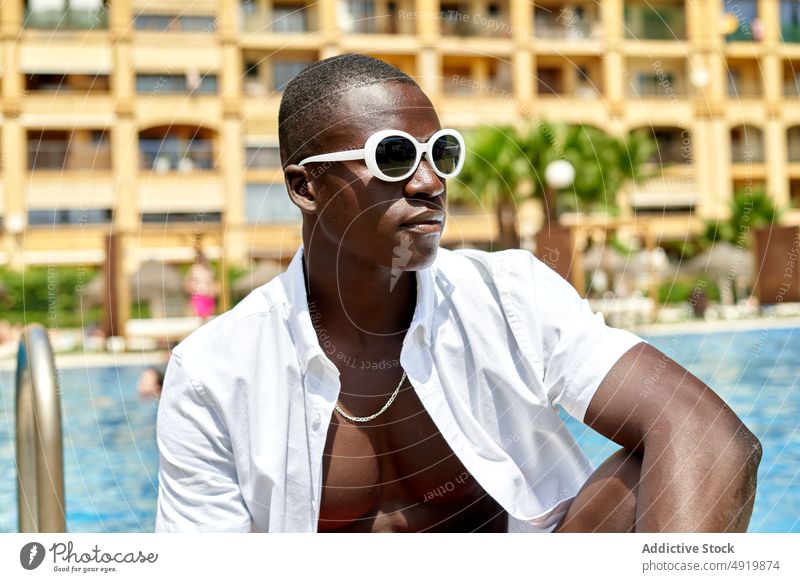 Schwarzer Mann sitzt am Pool ruhen Erholung Schwimmsport Beckenrand Kälte Zeitvertreib tropisch Resort Sonnenbrille schwarz Afroamerikaner reisen passen