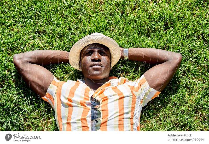Schwarzer Mann auf Rasen liegend ruhen sich[Akk] entspannen Sommer Feld verträumt Zeitvertreib Park Kälte Freizeit selbstbewusst Afroamerikaner schwarz Gras Hut