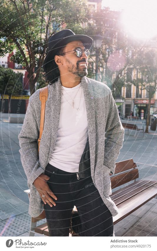 Stilvoller hispanischer Mann auf einer Straße in der Stadt Streetstyle urban tagsüber Outfit sonnenbeschienen Bank ruhen Vorschein männlich ethnisch Erwachsener