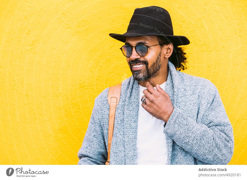 Glücklicher hispanischer Mann vor gelber Wand Streetstyle Lachen urban Outfit Vorschein hell Farbe männlich Erwachsener ethnisch Tasche Schulter heiter Stil