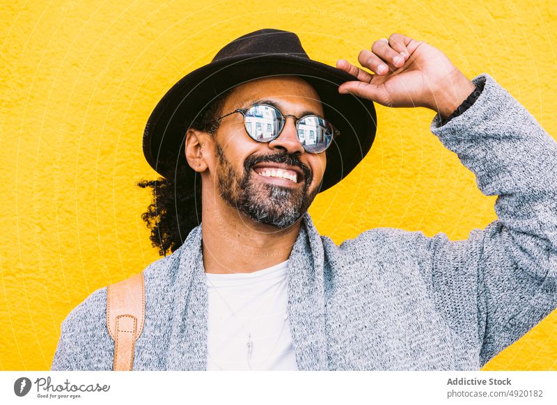 Glücklicher hispanischer Mann vor gelber Wand Streetstyle Lachen urban Outfit Vorschein hell Farbe männlich Erwachsener ethnisch Tasche Schulter heiter Stil