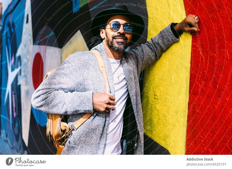 Stilvoller hispanischer Mann lehnt an einer Graffiti-Wand Lächeln Streetstyle positiv berühren urban Straße Gebäude männlich Erwachsener ethnisch Vorschein
