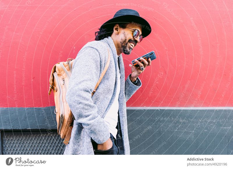 Stilvoller Mann, der eine Sprachnachricht auf der Straße aufnimmt Smartphone Stimme Nachricht senden Lächeln fettarm Wand Streetstyle ruhen männlich Erwachsener