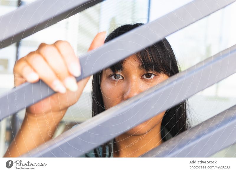 Asiatische Frau hinter grauem Zaun ruhen Straße berühren Windstille Gebäude urban dunkles Haar braunes Auge jung asiatisch ethnisch modern Individualität