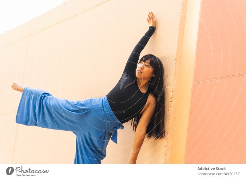 Barfüßige ethnische Tänzerin streckt sich auf der Straße Frau beweglich Wegbiegung Wand Straßenbelag Tanzen Dehnung Bein angehoben jung asiatisch Gleichgewicht