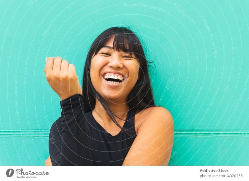 Glückliche asiatische Frau vor türkisfarbener Wand Lächeln urban Straße Stil Vorschein Porträt herzlich jung ethnisch lange Haare heiter froh tagsüber positiv