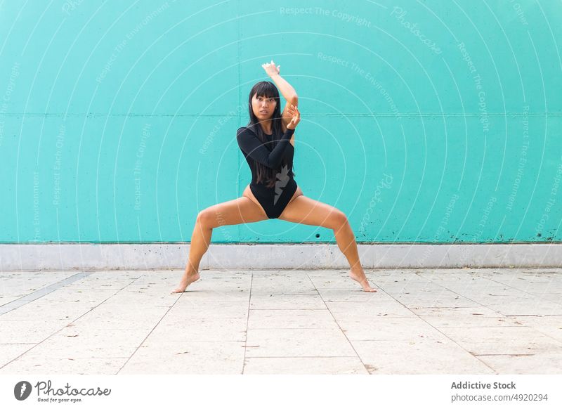 Asiatische Ballerina macht Plie Squat auf der Straße Frau Kniebeuge plie Anmut Tanzen ausführen Bürgersteig Wand beweglich jung asiatisch ethnisch Talent