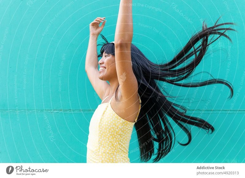Glückliche asiatische Frau beim Musikhören Tanzen Lächeln zuhören Wand urban Kopfhörer berühren meloman jung ethnisch Straße Stil Klang Audio Gerät Gesang froh
