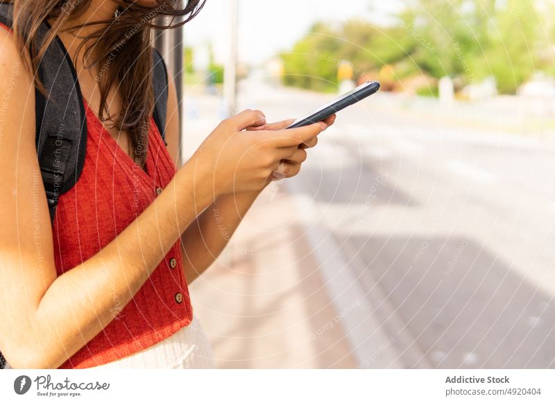 Anonyme Frau durchsucht Smartphone an Bushaltestelle Schüler Textnachricht warten Straße online Browsen Talkrunde urban Internet benutzend Rucksack Großstadt