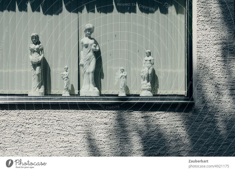 Weibliche Statuen aus Gips in einem Fenster vor Lamellen, rauh verputzte Wand und Schatten weiblich Sonne Putz Kunst griechisch kurios Standbilder Schönheit