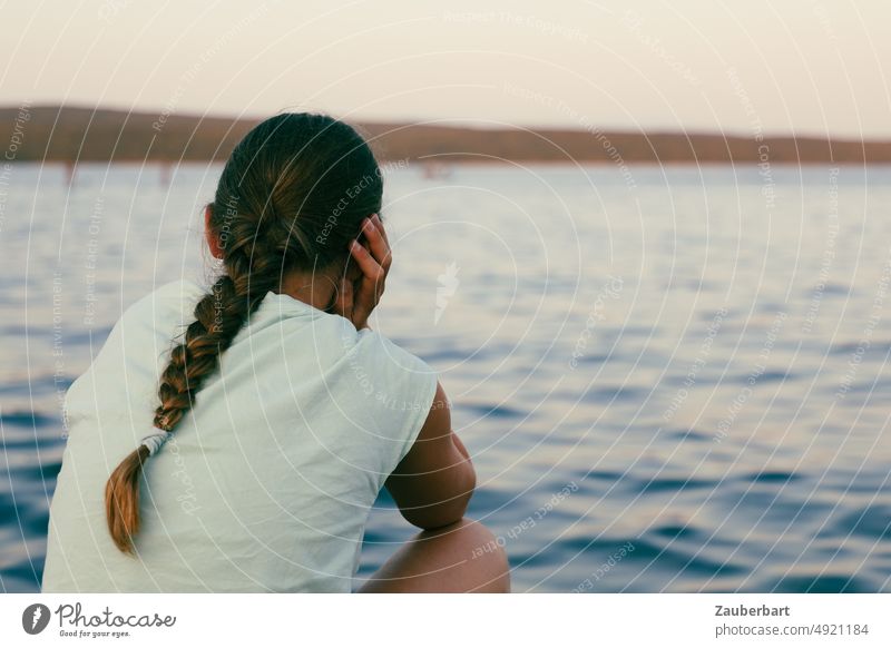 Mädchen mit Zopf sitzt gedankenverloren am Meer Gedanken Abend Ausblick nachdenklich schauen Zukunft Schicksal grübeln denken nachdenken Wellen Wasser Gefühle