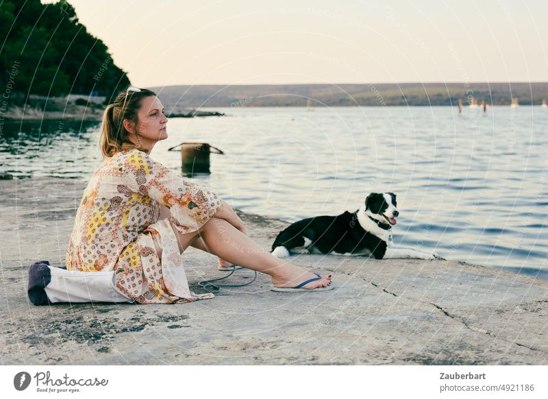 Frau im Sommerkleid sitzt mit ihrem Hund am Meer Touristin schauen Abend Ruhe genießen nachdenklich denken Freunde Tierliebe Natur Küste Wasser Urlaub