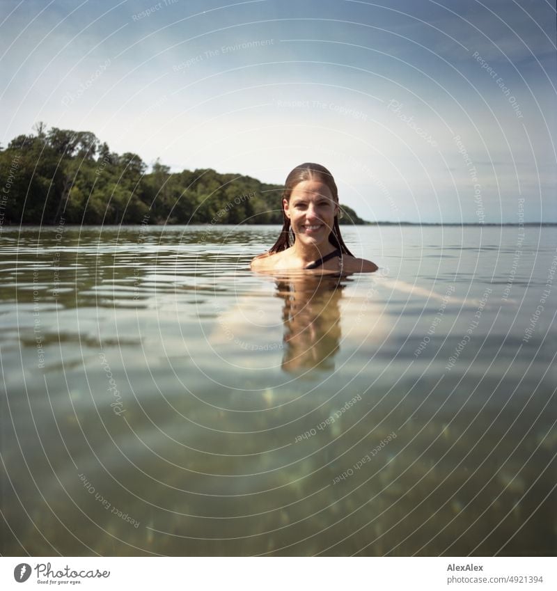 Junge, schöne Frau im flachen Wasser in der Ostsee schaut in die Kamera und lächelt Lifestyle Gegenlicht gesund sportlich schlank ästhetisch jugendlich anmutig