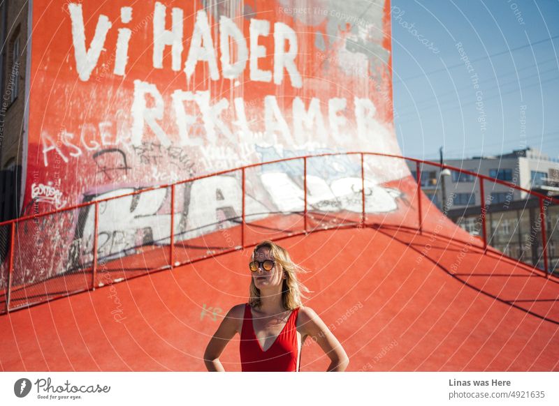 Es ist heiß in der Stadt Kopenhagen, Dänemark. Ein heißes blondes Mädchen in einem roten Badeanzug steht stolz hinter einem roten Skatepark mit Graffiti und Tags. Der Sommer in der Stadt könnte auch abenteuerlich sein.
