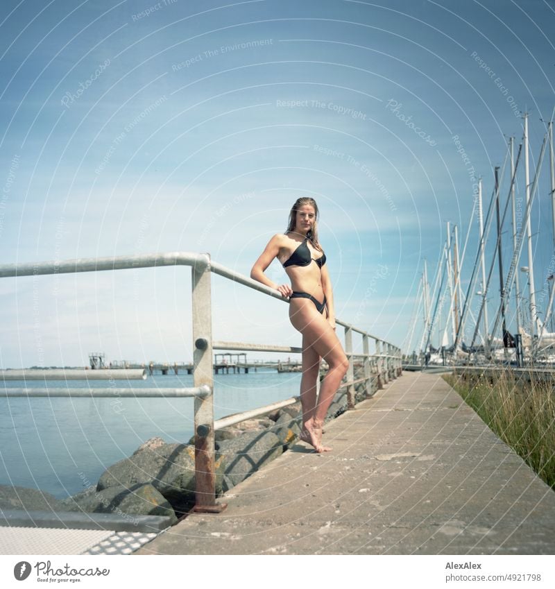 Analoges Mittelformatbild einer jungen, schönen, großen Frau im Bikini am Pier an der Ostsee Lifestyle gesund sportlich schlank ästhetisch jugendlich anmutig