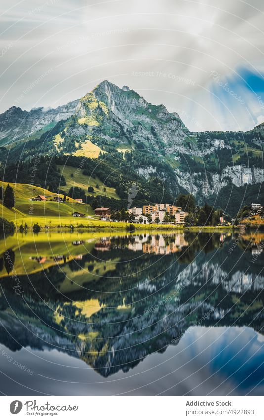 Malerische Landschaft mit ruhigem See, in dem sich Berge und Häuser spiegeln Berge u. Gebirge Natur Dorf Cottage Tal malerisch Hochland Wohnsiedlung