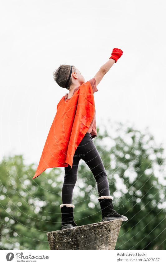 Anonymer Superheld in Igelmaske im Park mit erhobenen Armen und geballter Faust Junge Mundschutz spielen Aufstieg Tracht so tun, als ob knien Stein Klotz Mut