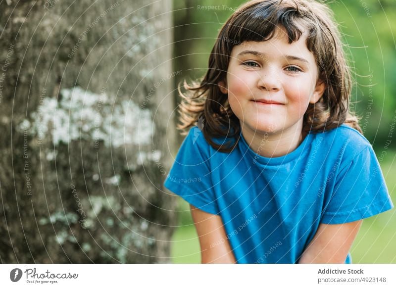 Niedliches kleines Mädchen in der Nähe des Baumes Park Lächeln Wochenende Sommer ruhen Kofferraum Porträt niedlich wenig Kind lässig T-Shirt dunkles Haar