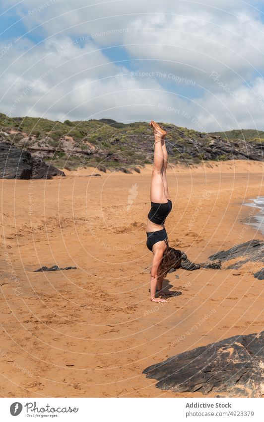 Frau macht Handstand gegen Hügel Yoga Sommer Gleichgewicht Stein Strand Zen Sitzung Meer Küste Wohlbefinden Ufer Blauer Himmel üben Asana Wasser Barfuß