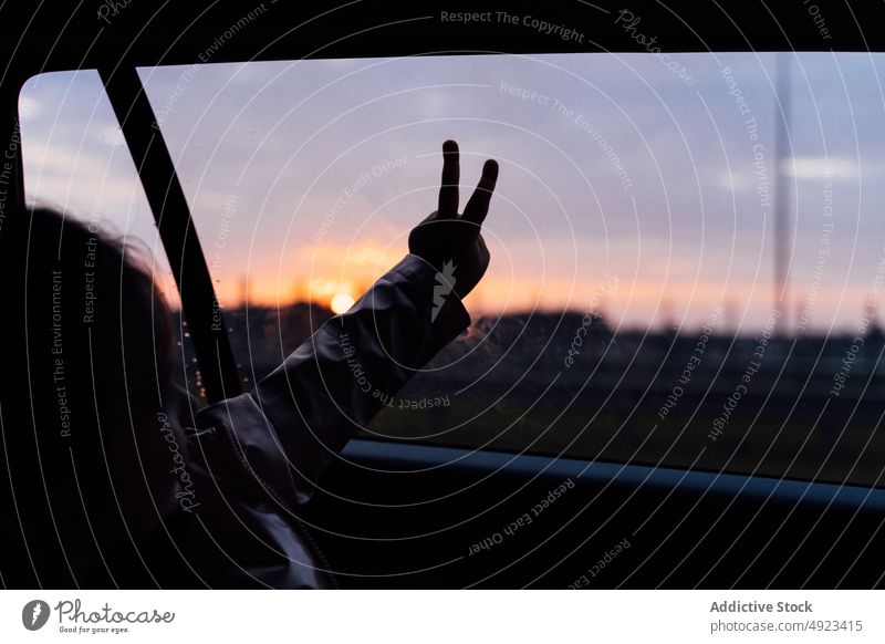 Crop Kind macht Frieden Geste auf Autofenster während der Reise PKW Fenster gestikulieren Autoreise Landschaft Mitfahrgelegenheit bewundern Automobil Passagier