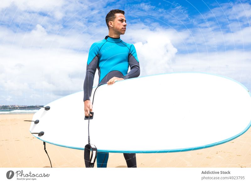 Junger ethnischer Mann hält Surfbrett am Meeresufer Surfer Strand Athlet selbstbewusst hawaiianisch nachdenklich besinnlich lose hängen männlich Halt jung