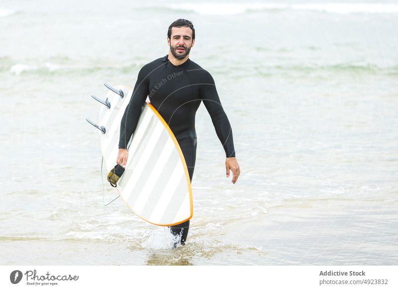 Männlicher Surfer, der vor dem Reiten einer Welle ins Meer geht Mann Surfbrett Spaziergang Sport sportlich Feiertag genießen Gesundheit Zeit verbringen jung