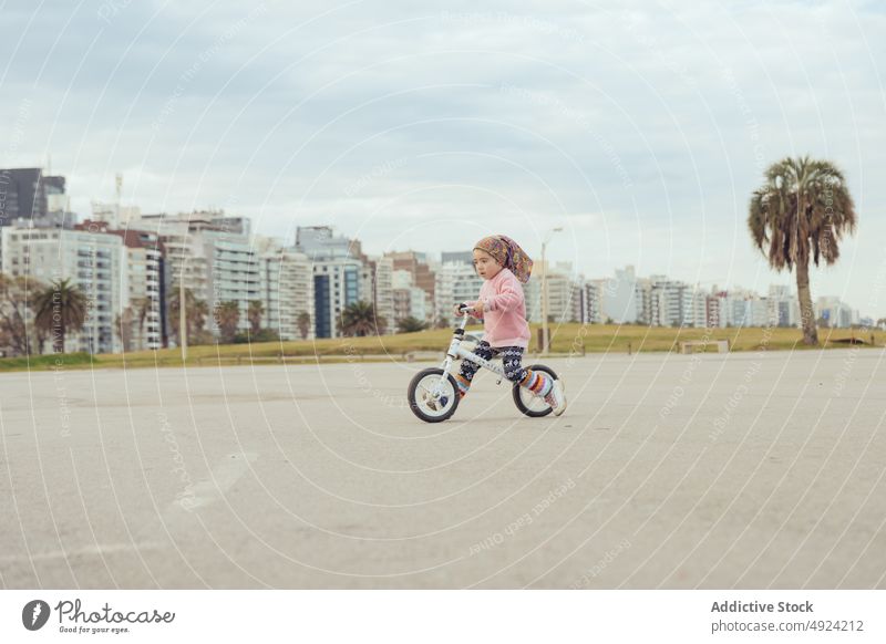 Mädchen fährt Fahrrad auf der Straße Mitfahrgelegenheit Gleichgewicht urban Wochenende wolkig Himmel Appartement Gebäude grau Weg sich[Akk] bewegen Kind lässig