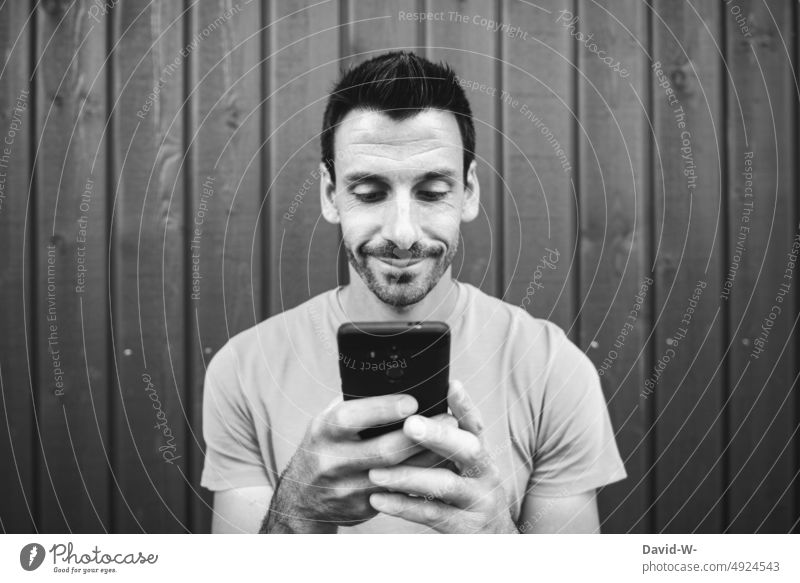 Mann mit dem Handy in den Händen am tippen lächeln zufrieden benutzen erfolgreich grinsen smartphone