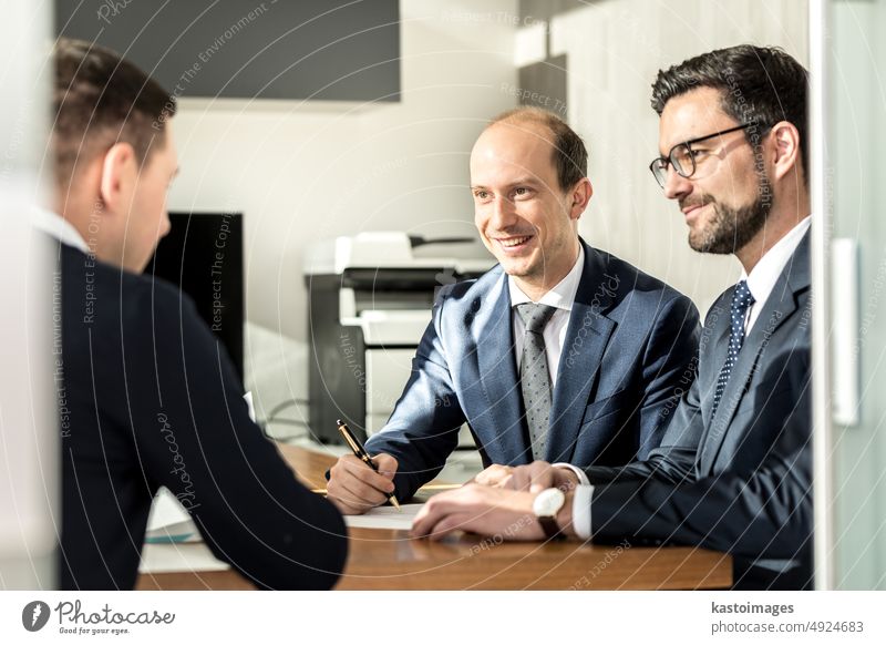 Eine Gruppe selbstbewusster, erfolgreicher Geschäftsleute, die bei einem Geschäftstreffen in einem modernen Büro einen Vertrag besprechen und unterzeichnen, um das Geschäft zu besiegeln.